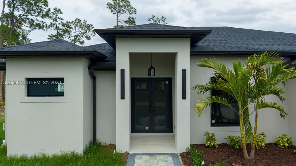 The exterior of a modern house features a covered entryway with double glass doors — 814 Calyton Ave, Lehigh Acres FL 33972, LEHIGH ACRES, FL