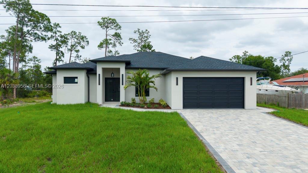 A modern single-story house with a dark roof, light stucco exterior, and a paved driveway — 814 Calyton Ave, Lehigh Acres FL 33972, LEHIGH ACRES, FL