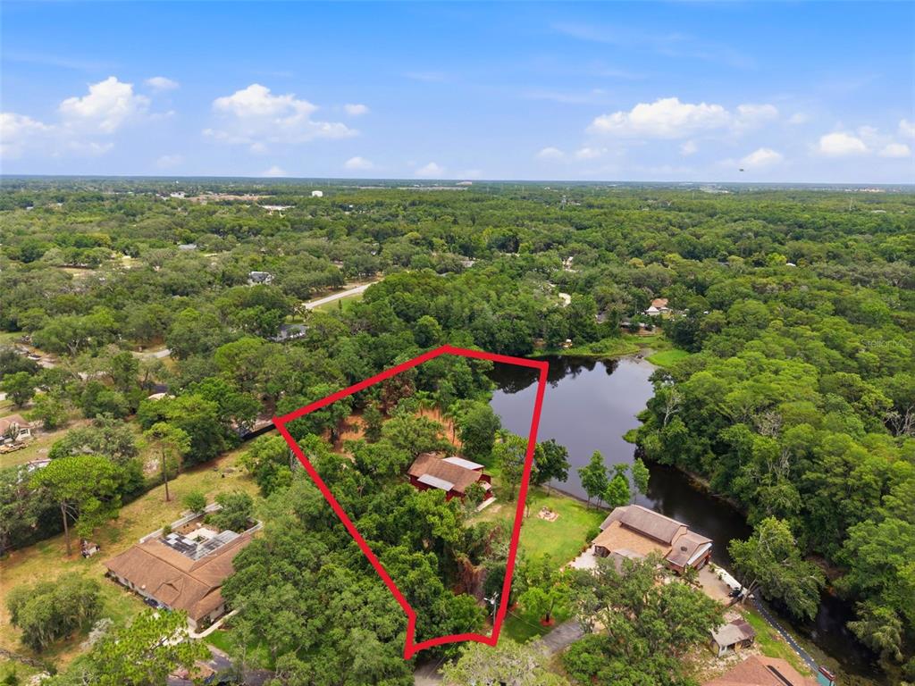 An aerial view shows a house on a wooded lot bordering a small lake — 6409 CHISWICK COURT, NEW PORT RICHEY, FL