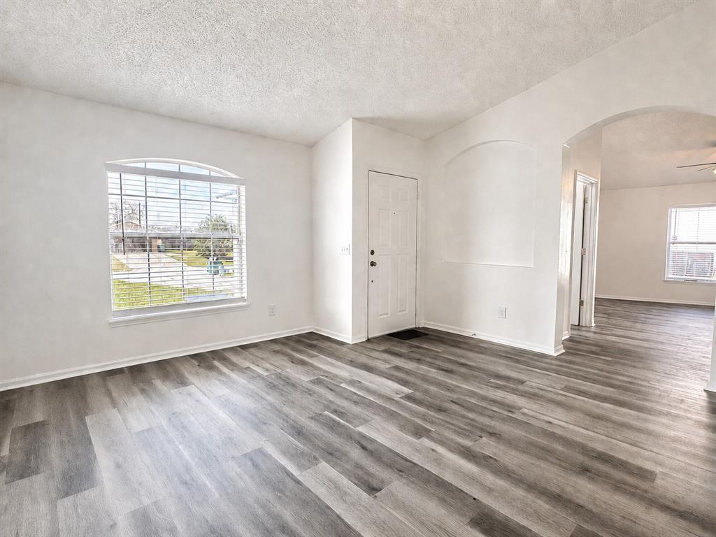 An empty living room features gray wood-look flooring, white walls, and an arched entryway — 2871 LOCKWOOD BOULEVARD, DELTONA, FL