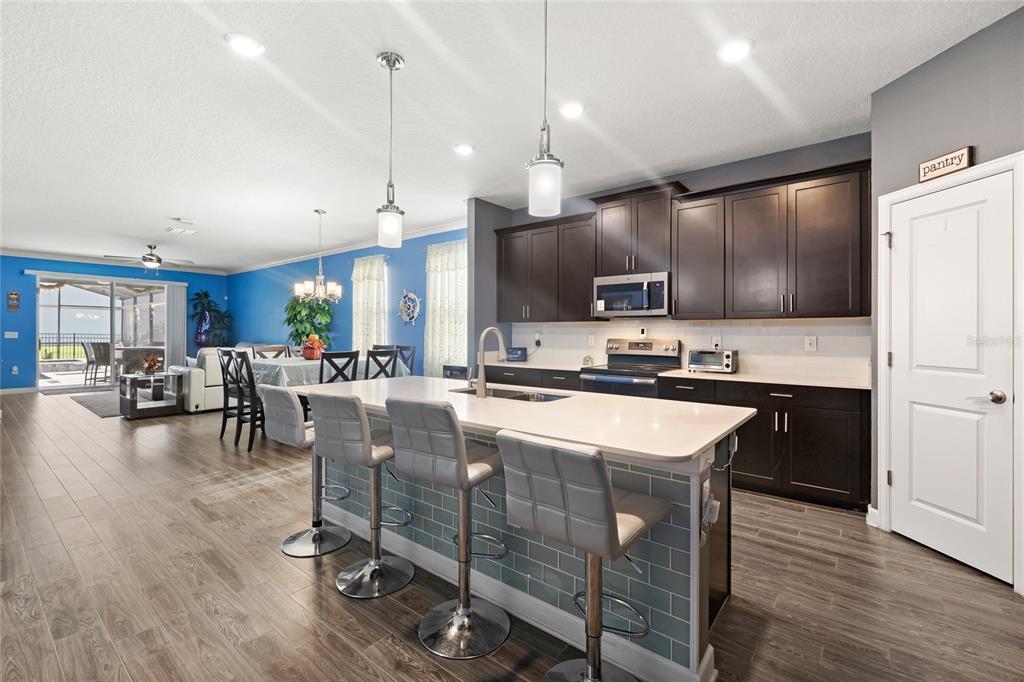 A kitchen with dark cabinets, a quartz island with bar stools, and an adjacent dining area — 12073 IMAGINARY WAY, ORLANDO, FL