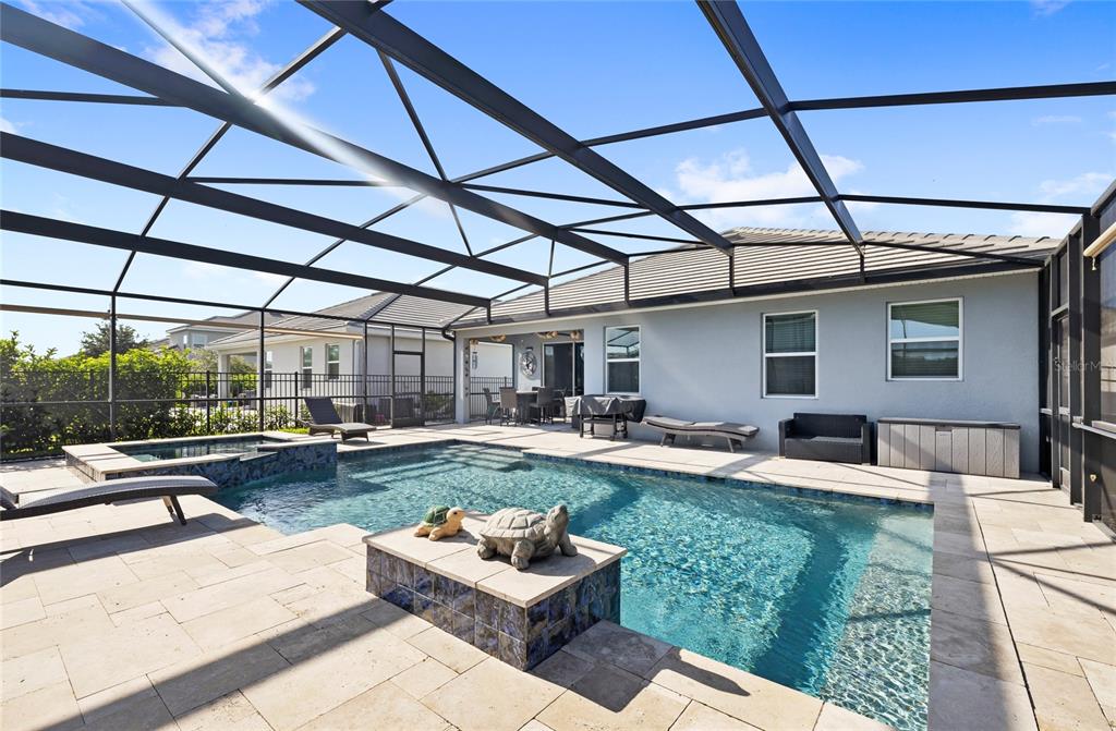 A screened-in patio features a swimming pool with a spa and stone tile decking — 12073 IMAGINARY WAY, ORLANDO, FL