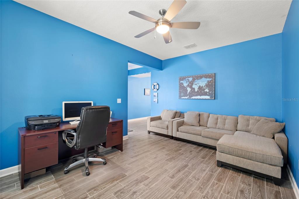 A home office features blue walls, a desk with a chair, and a sectional sofa — 12073 IMAGINARY WAY, ORLANDO, FL
