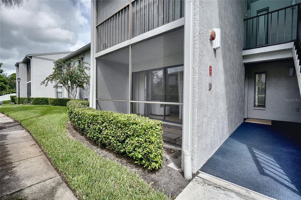 A ground-floor apartment unit features a screened-in patio, a blue entryway mat, and landscaping — 1716 PINE RIDGE ROAD UNIT F1, SANFORD, FL