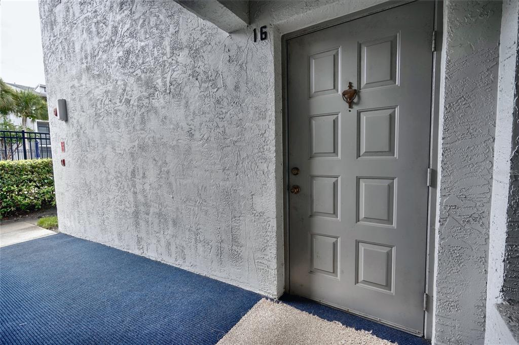 A gray door marked with the number 16 sits on a textured wall with blue carpeting — 1716 PINE RIDGE ROAD UNIT F1, SANFORD, FL