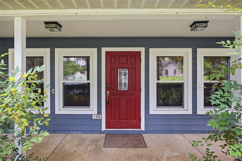 A red front door is centered between four windows on a blue-sided porch — 155 SE 32ND PLACE, OCALA, FL