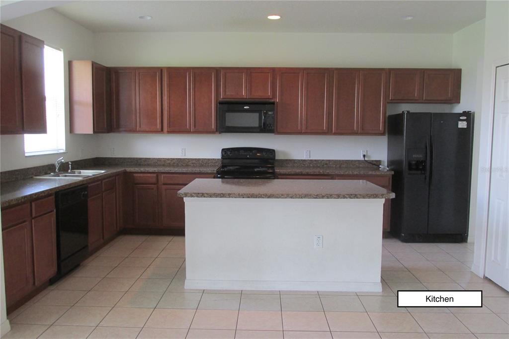 A kitchen with brown cabinets, granite countertops, a center island, and black appliances — 3838 GOLDEN KNOT DRIVE, KISSIMMEE, FL