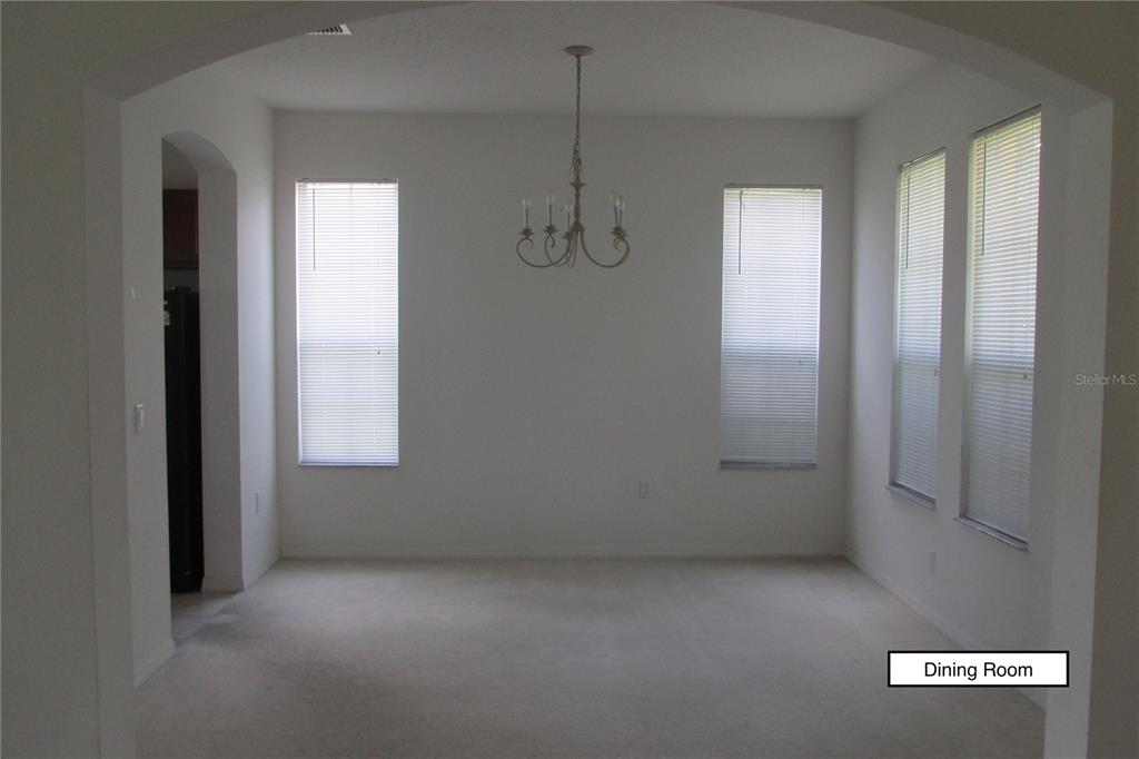A dining room features white walls, beige carpeting, a chandelier, and four windows with blinds — 3838 GOLDEN KNOT DRIVE, KISSIMMEE, FL