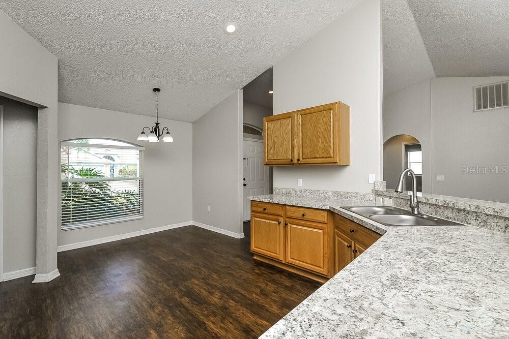 A kitchen with wood cabinets and granite countertops overlooks a dining area with wood flooring — 6025 LIVE OAK DRIVE, WINTER HAVEN, FL