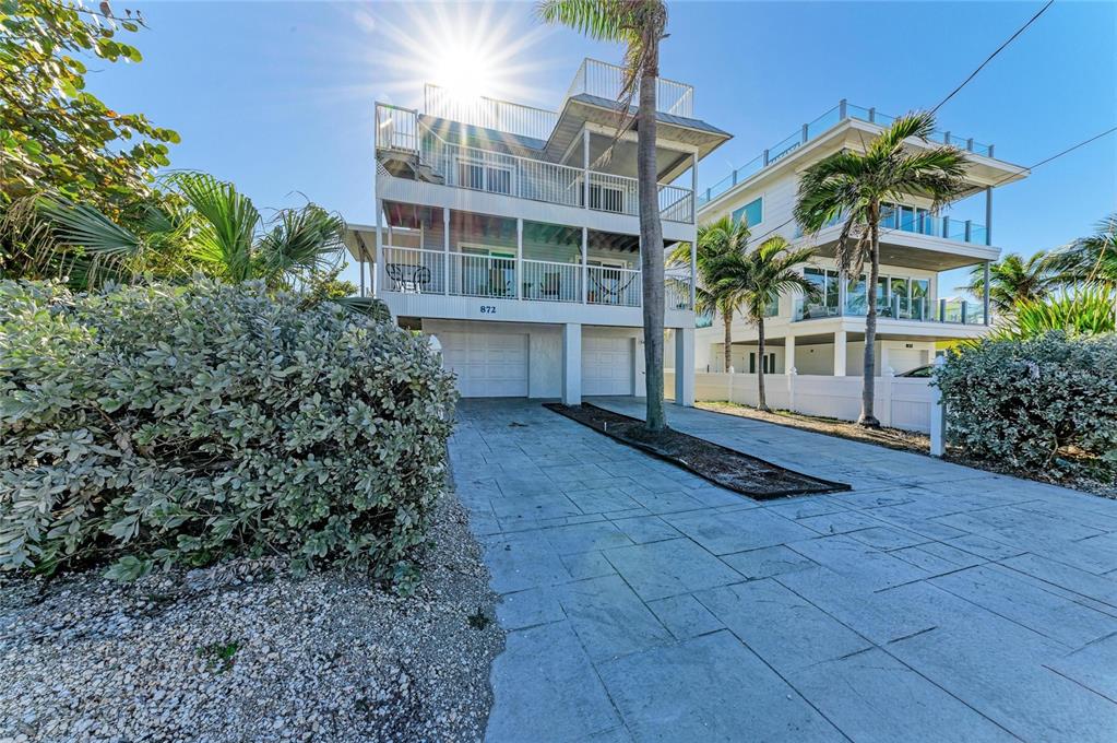 A three-story coastal house with a paved driveway and balconies under a bright sun — 872 NORTH SHORE DRIVE, ANNA MARIA, FL