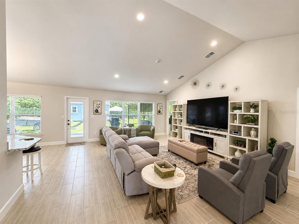 A living room features light tile floors, a vaulted ceiling, and a large television console — 4869 SW 115TH STREET, OCALA, FL