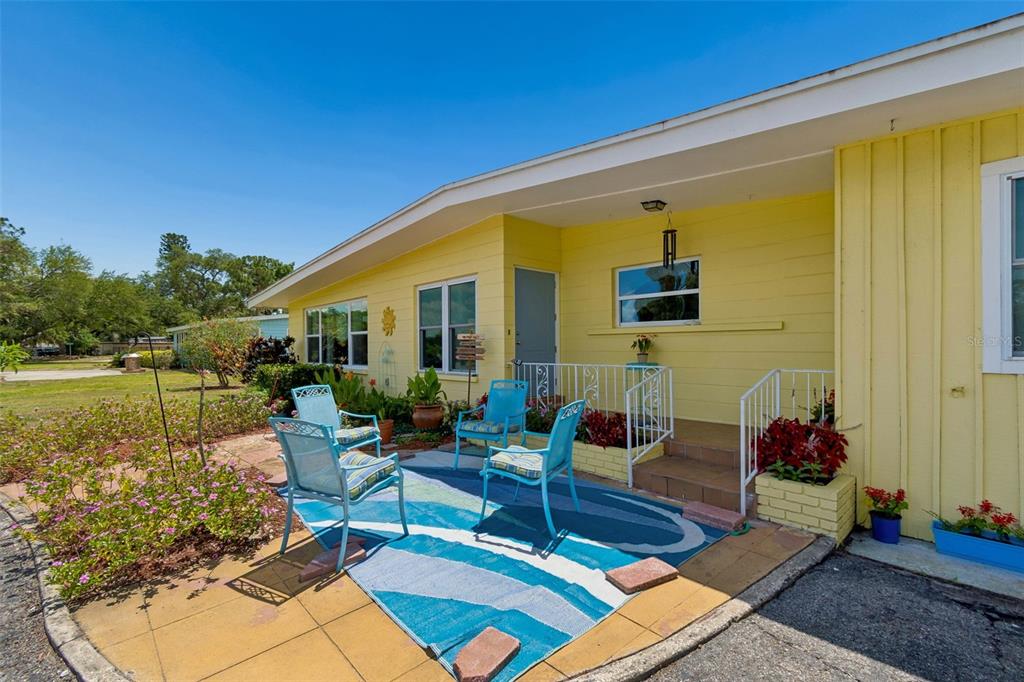 A yellow house exterior features a patio with blue chairs and a patterned outdoor rug — 2110 FAIRWAY AVENUE S, ST PETERSBURG, FL