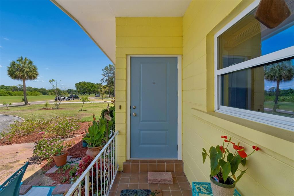 A blue front door is set into a yellow exterior wall on a tiled porch — 2110 FAIRWAY AVENUE S, ST PETERSBURG, FL