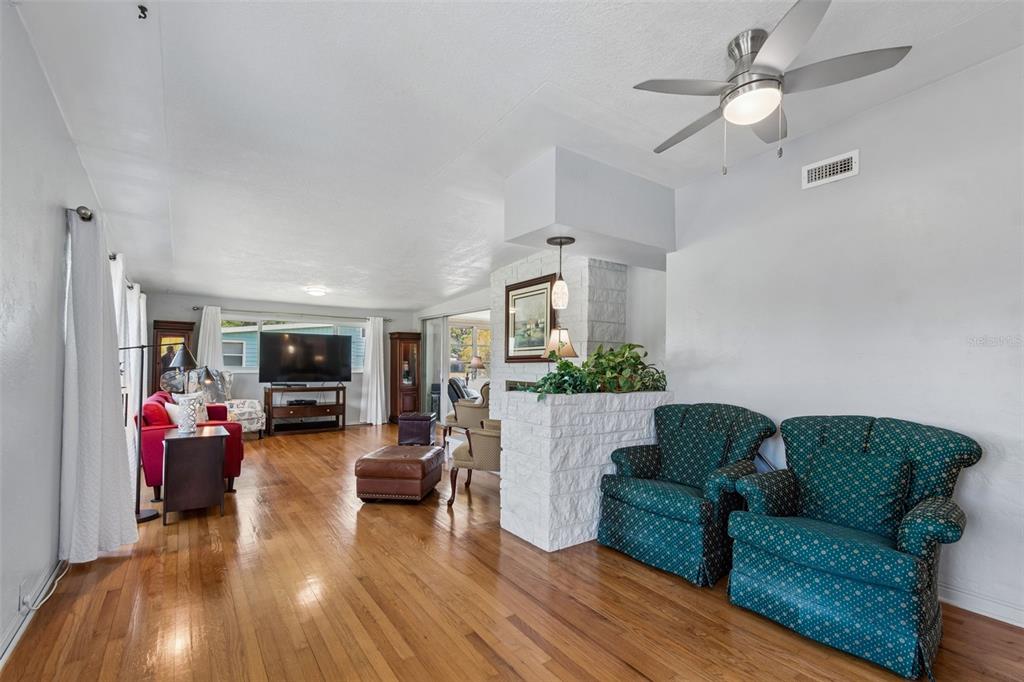 A living room features hardwood floors, a white brick fireplace divider, and two patterned armchairs — 2110 FAIRWAY AVENUE S, ST PETERSBURG, FL
