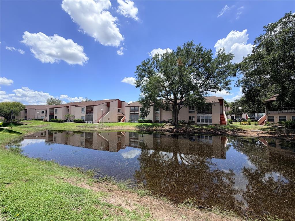 A pond reflects a multi-story apartment complex with trees under a blue sky — 2562 LAKEWAY BRANCH DRIVE UNIT 3002, ORLANDO, FL
