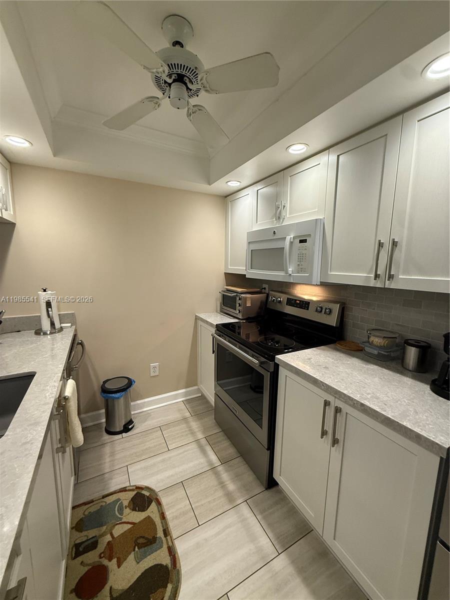 A galley kitchen features white cabinets, light countertops, stainless steel appliances, and tile flooring — 608 Waterside Dr # 608, Hypoluxo FL 33462, HYPOLUXO, FL