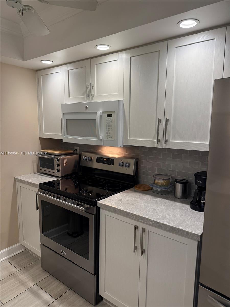 A kitchen features white cabinets, stainless steel appliances, and a gray tiled backsplash — 608 Waterside Dr # 608, Hypoluxo FL 33462, HYPOLUXO, FL