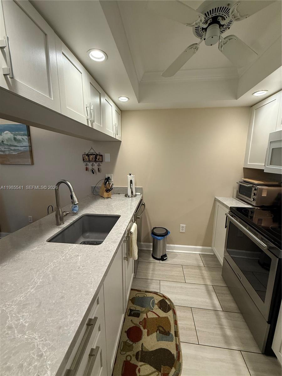A galley kitchen features white cabinets, light-colored countertops, stainless steel appliances, and tile flooring — 608 Waterside Dr # 608, Hypoluxo FL 33462, HYPOLUXO, FL
