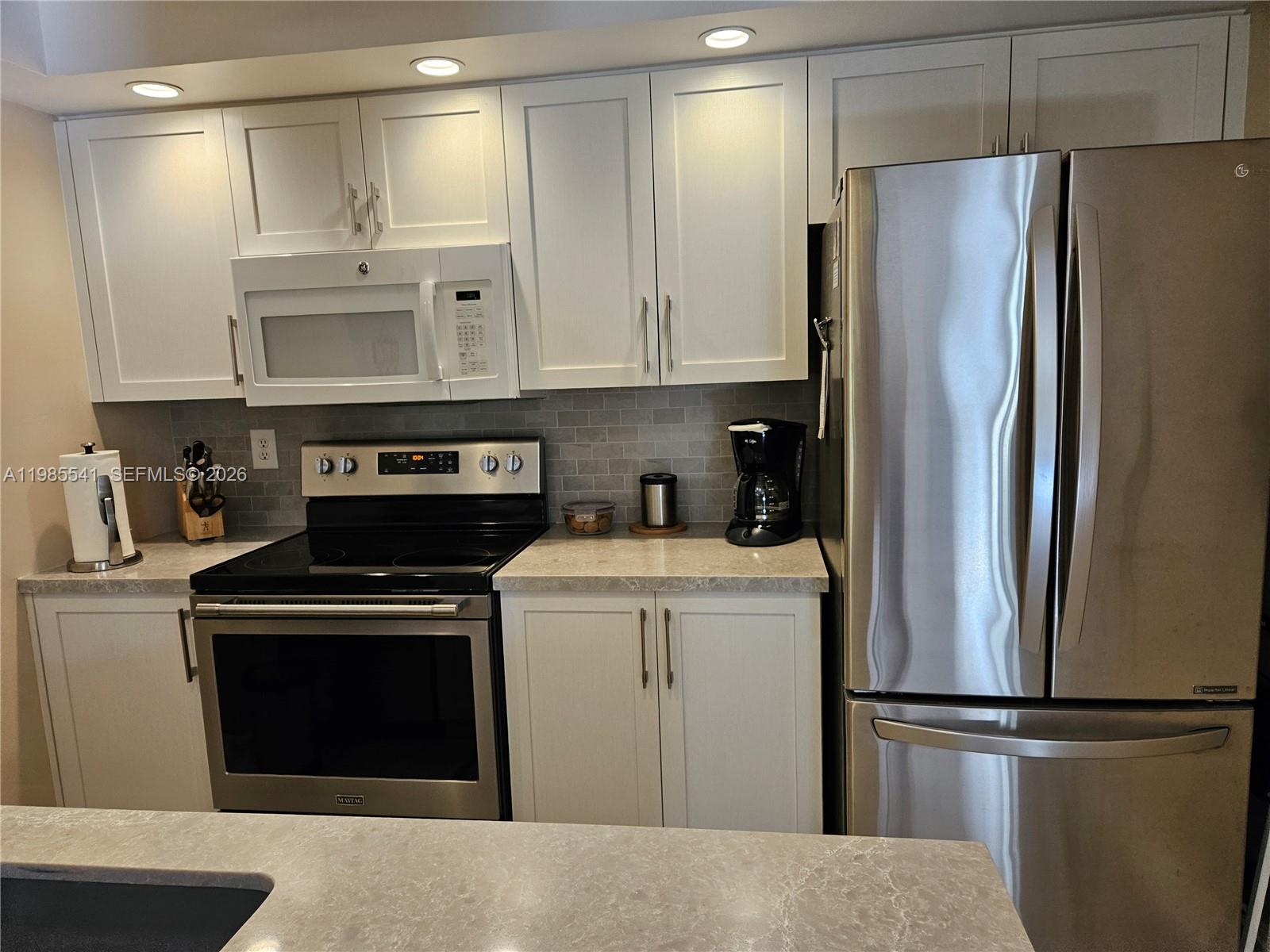 A kitchen features white cabinets, stainless steel appliances, and a gray tiled backsplash — 608 Waterside Dr # 608, Hypoluxo FL 33462, HYPOLUXO, FL