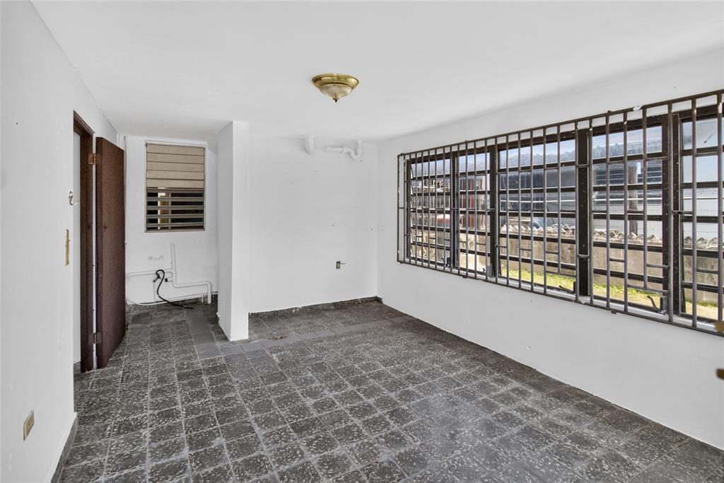 An empty room with dark tiled flooring, white walls, and windows covered by metal security bars — 3 URBANIZACIÓN REPARTO MARQUEZ UNIT BLQ B7, ARECIBO, PR