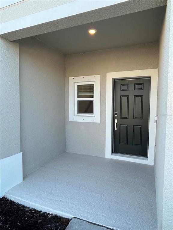 A covered concrete porch features a black front door and a small window with trim — 5845 BISCOTTI ST, NOKOMIS, FL