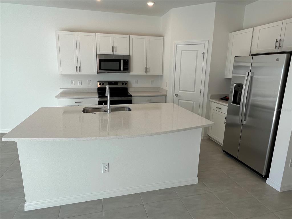 A kitchen features a large quartz island, white cabinets, and stainless steel appliances — 5845 BISCOTTI ST, NOKOMIS, FL