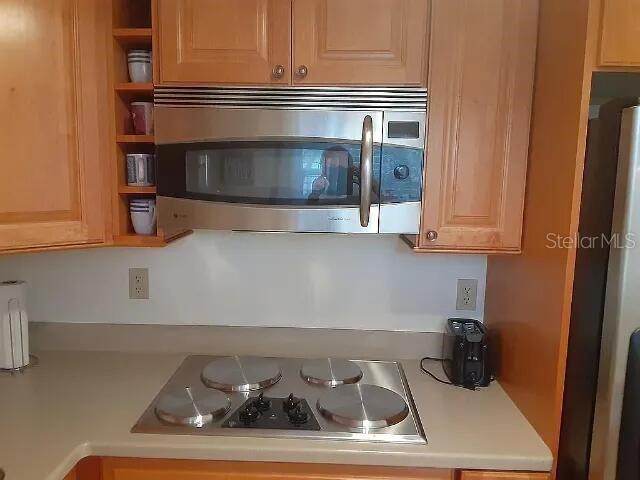 A kitchen features a stainless steel microwave above a four-burner electric cooktop and wooden cabinets — 94 SPRING LAKE DRIVE UNIT 203, VERO BEACH, FL