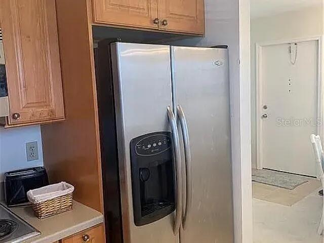 A stainless steel refrigerator stands in a kitchen next to wooden cabinets and a doorway — 94 SPRING LAKE DRIVE UNIT 203, VERO BEACH, FL