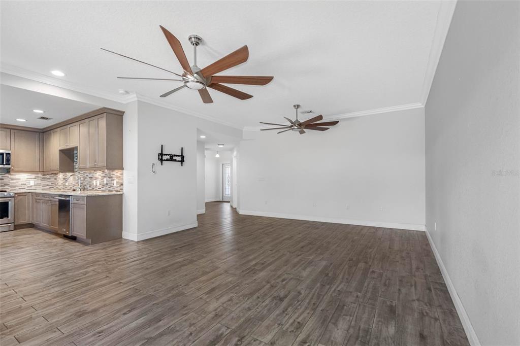 An open-concept living area with wood-look tile flooring, two ceiling fans, and an adjacent kitchen — 763 DATE PALM LANE, ST PETERSBURG, FL