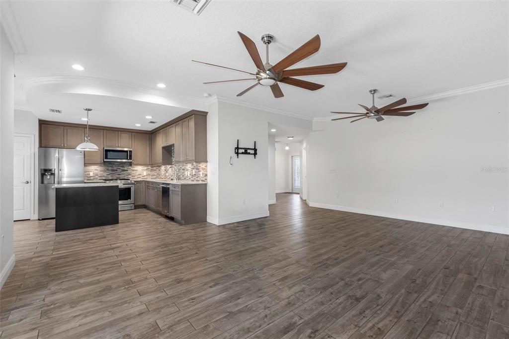 An open-concept kitchen and living area with wood-look tile flooring and two ceiling fans — 763 DATE PALM LANE, ST PETERSBURG, FL
