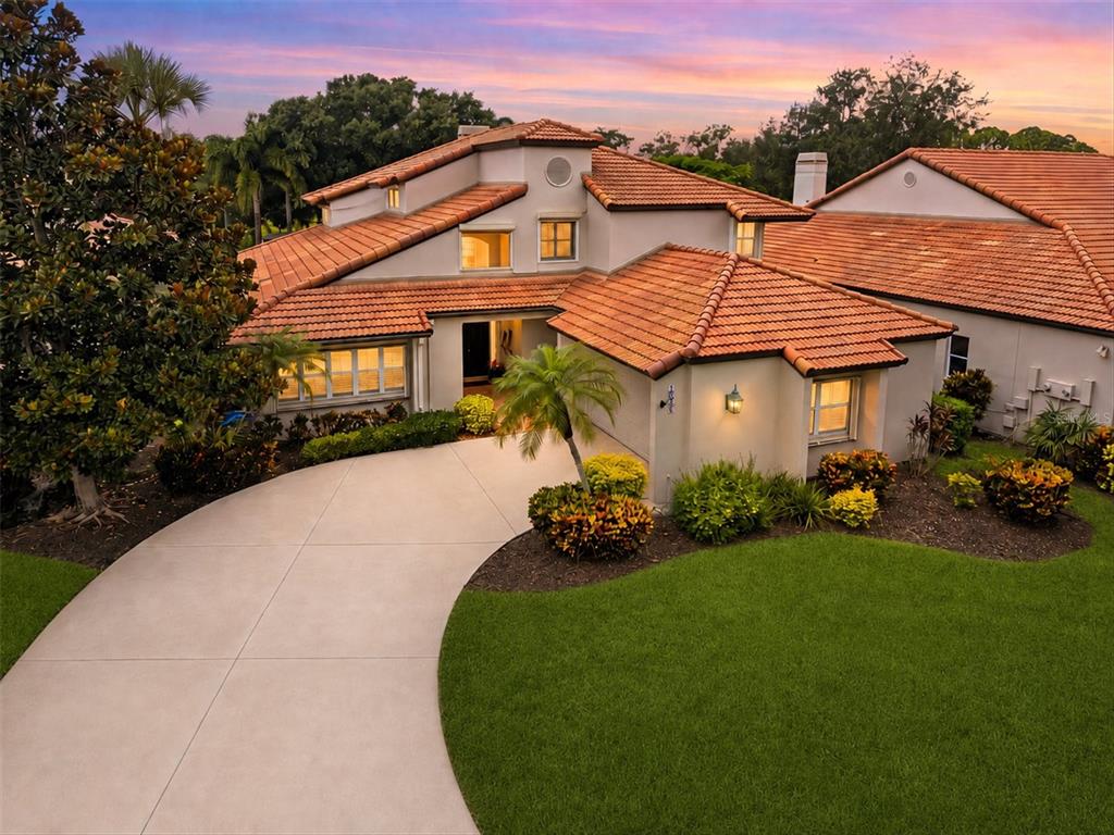 An exterior view of a two-story house with a tile roof and a curved driveway — 7596 CALLE FACIL, SARASOTA, FL