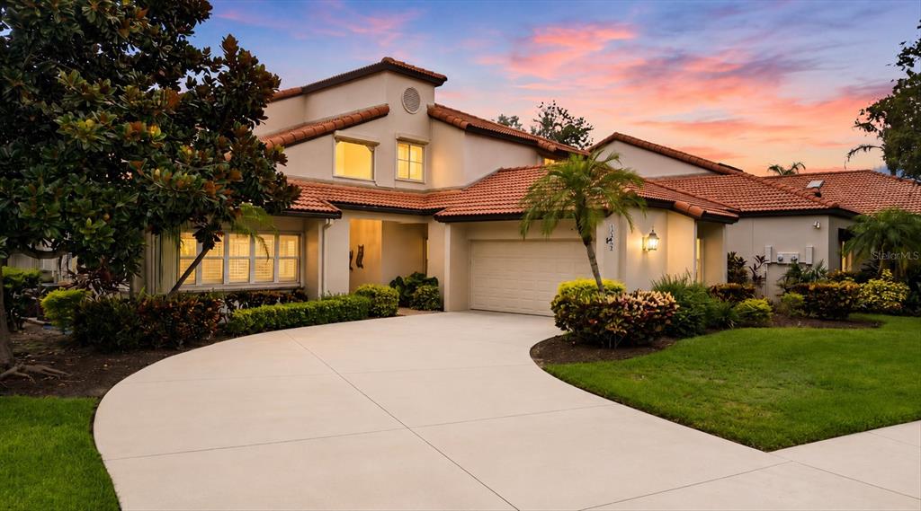 A two-story house with a tile roof, beige stucco exterior, and a curved concrete driveway — 7596 CALLE FACIL, SARASOTA, FL