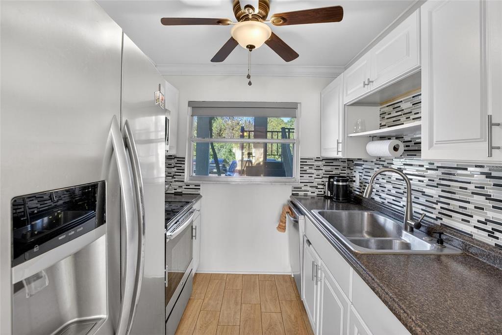 A galley kitchen features stainless steel appliances, white cabinets, a tiled backsplash, and wood-look flooring — 1303 S HERCULES AVENUE UNIT 2, CLEARWATER, FL