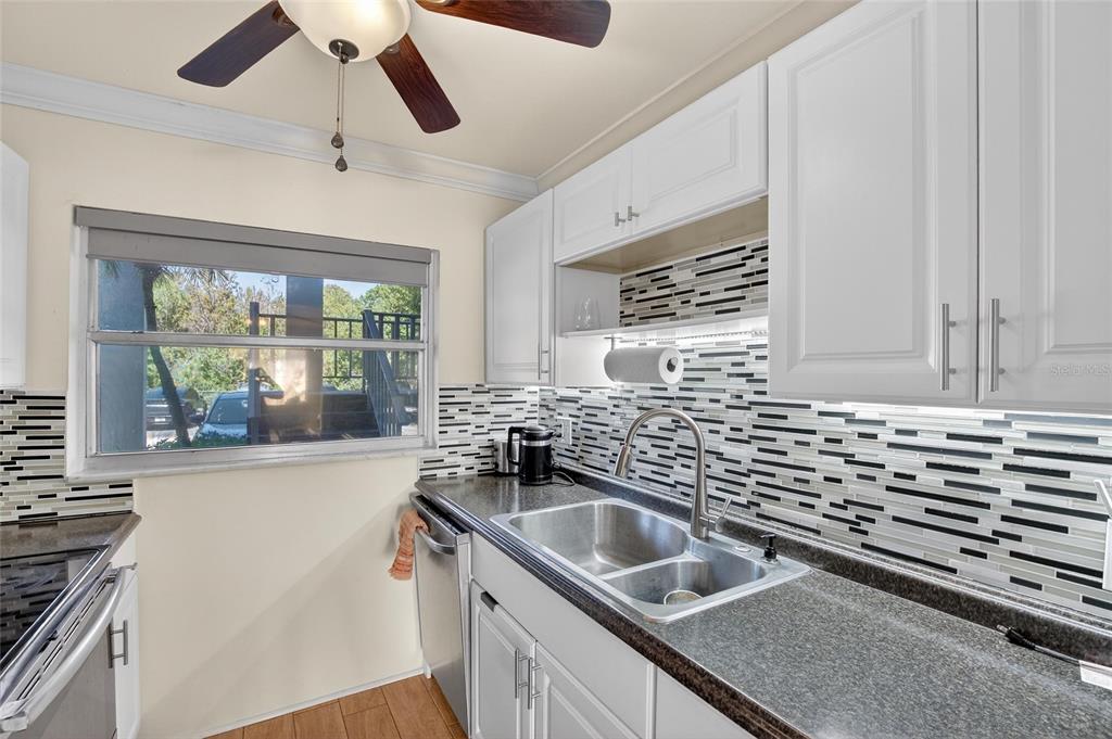 A kitchen features white cabinets, a dark granite countertop, a double sink, and tiled backsplash — 1303 S HERCULES AVENUE UNIT 2, CLEARWATER, FL