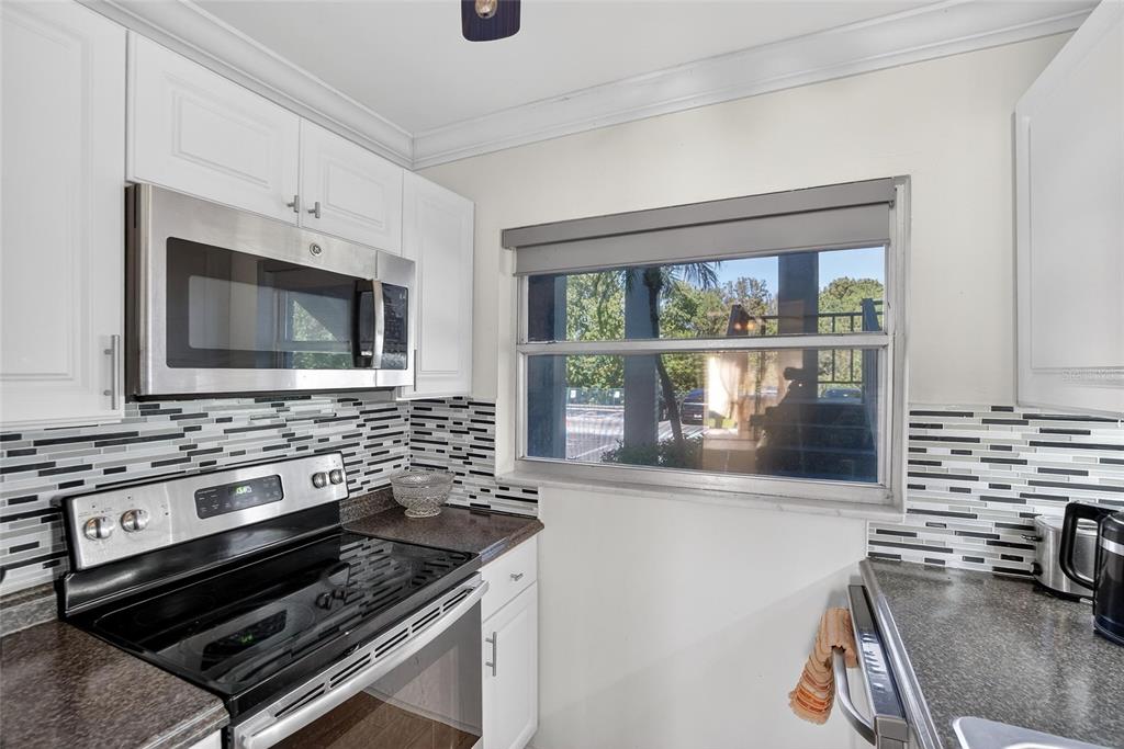 A kitchen features white cabinets, stainless steel appliances, a mosaic tile backsplash, and a window — 1303 S HERCULES AVENUE UNIT 2, CLEARWATER, FL