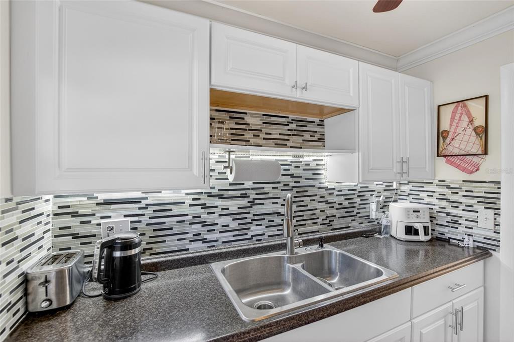 A kitchen features white cabinets, a dark granite countertop, a double sink, and tiled backsplash — 1303 S HERCULES AVENUE UNIT 2, CLEARWATER, FL