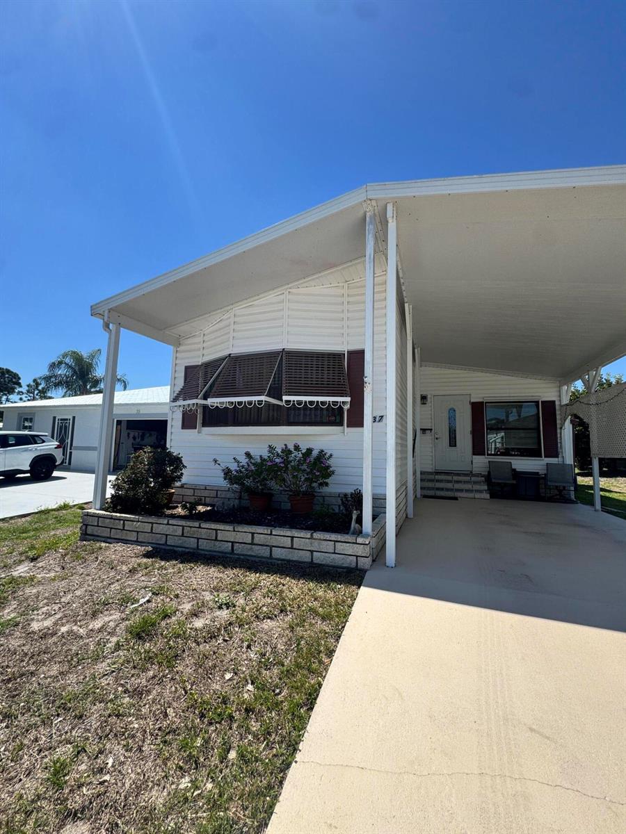A white mobile home with a carport, a brick planter, and a bay window — 37 San Roberto, Fort Pierce FL 34951, FORT PIERCE, FL