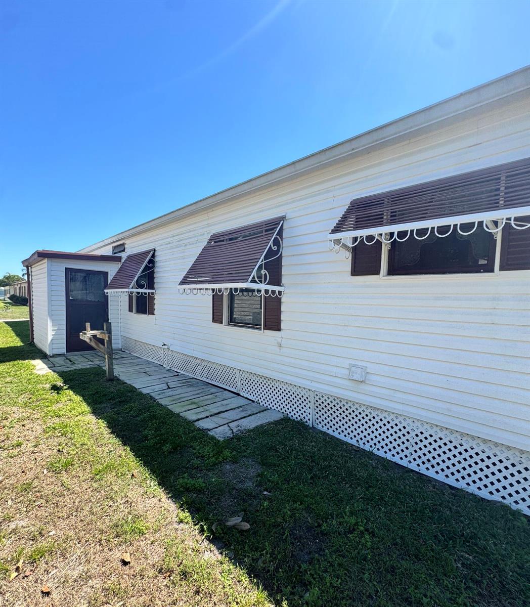 The exterior of a white mobile home features brown window awnings and lattice skirting — 37 San Roberto, Fort Pierce FL 34951, FORT PIERCE, FL