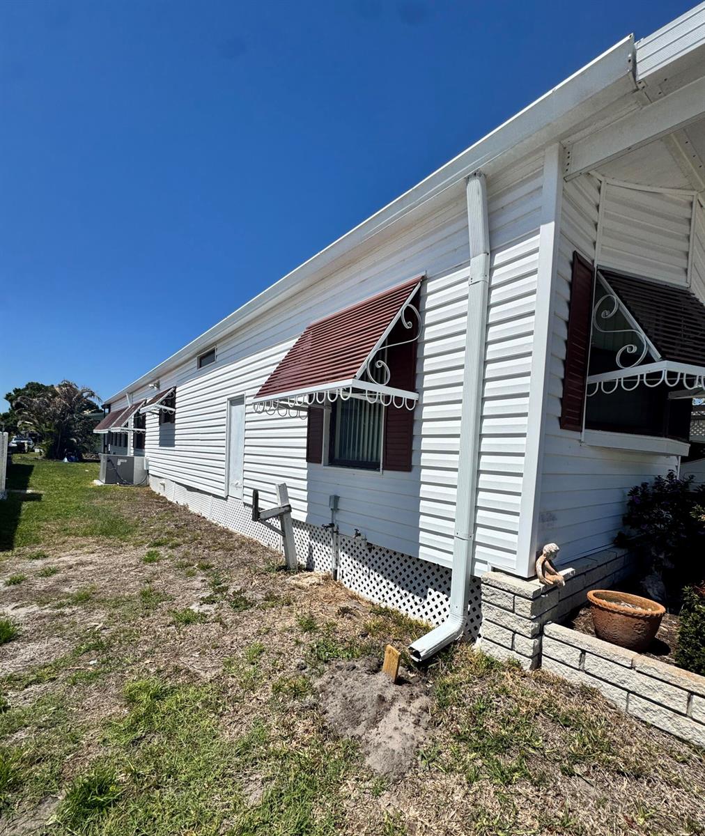 The exterior side of a white mobile home features red window awnings and a downspout — 37 San Roberto, Fort Pierce FL 34951, FORT PIERCE, FL