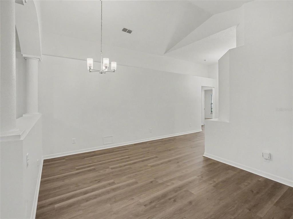 An empty dining room features a vaulted ceiling, a modern chandelier, and wood-look flooring — 2218 BRACKNELL FOREST TRAIL, TAVARES, FL