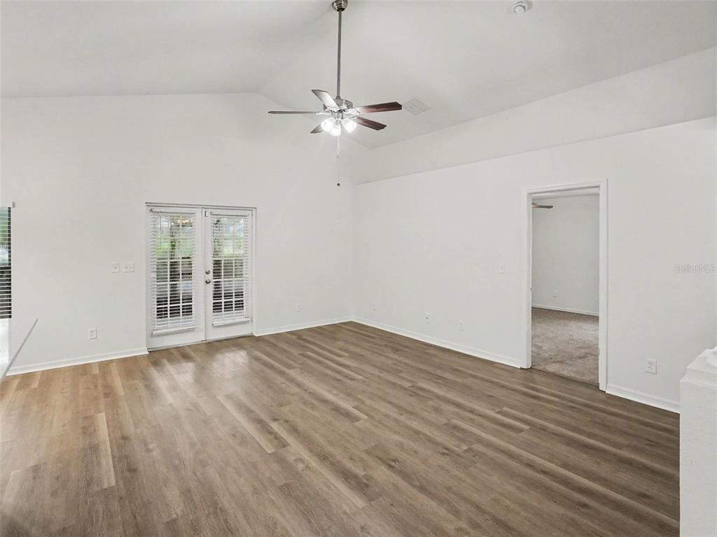 A bright living room features vaulted ceilings, wood-look flooring, a ceiling fan, and French doors — 2218 BRACKNELL FOREST TRAIL, TAVARES, FL