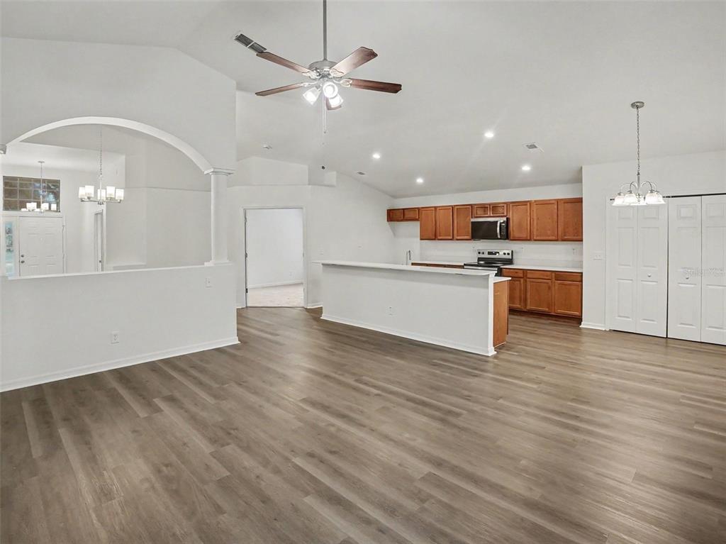 An open-concept living area features wood-look flooring, a kitchen with wood cabinets, and vaulted ceilings — 2218 BRACKNELL FOREST TRAIL, TAVARES, FL