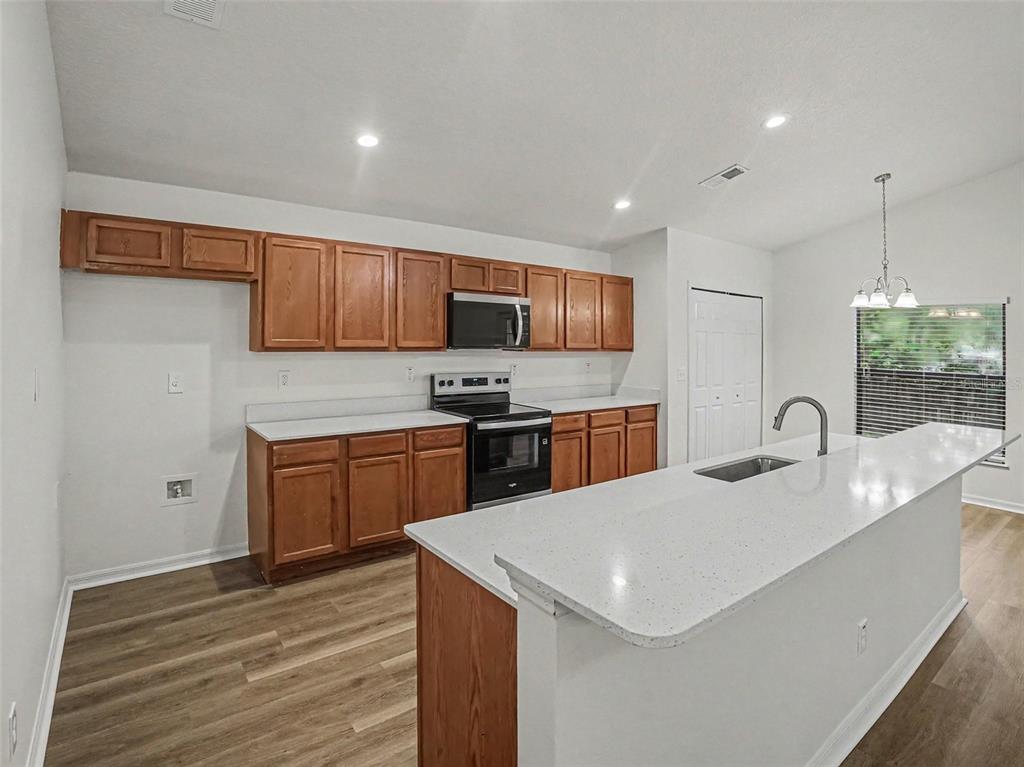 A kitchen features wood cabinets, white countertops, stainless steel appliances, and a central island — 2218 BRACKNELL FOREST TRAIL, TAVARES, FL