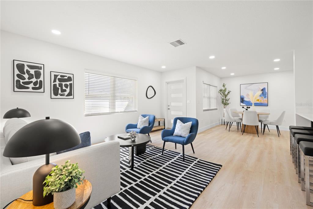 An open-concept living and dining area features light wood flooring, blue accent chairs, and modern decor — 2117 S WEST SHORE BOULEVARD, TAMPA, FL