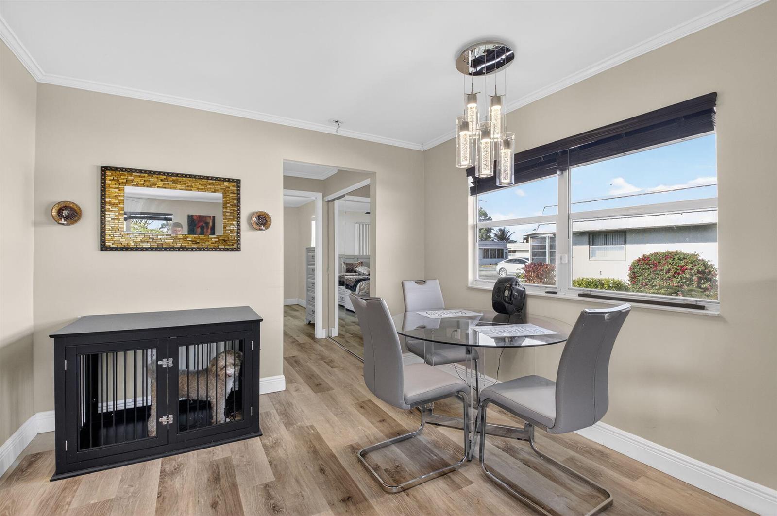 A dining area features a glass table, grey chairs, wood-look flooring, and a dog crate — 170 Valencia H, Delray Beach FL 33446, DELRAY BEACH, FL