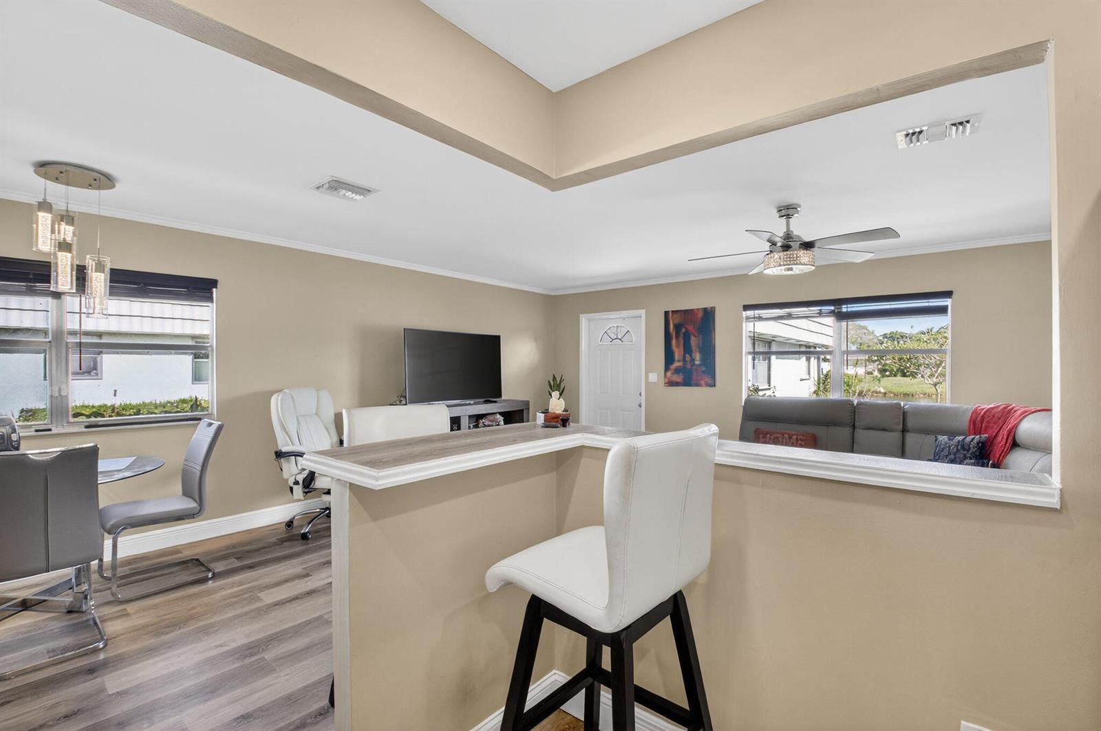 A kitchen breakfast bar overlooks a living room with a gray sofa and ceiling fan — 170 Valencia H, Delray Beach FL 33446, DELRAY BEACH, FL