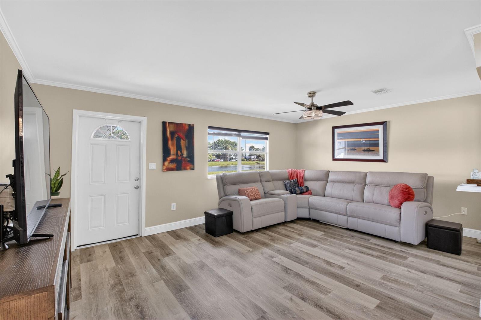 A living room features a grey sectional sofa, wood-look flooring, and a view of water — 170 Valencia H, Delray Beach FL 33446, DELRAY BEACH, FL