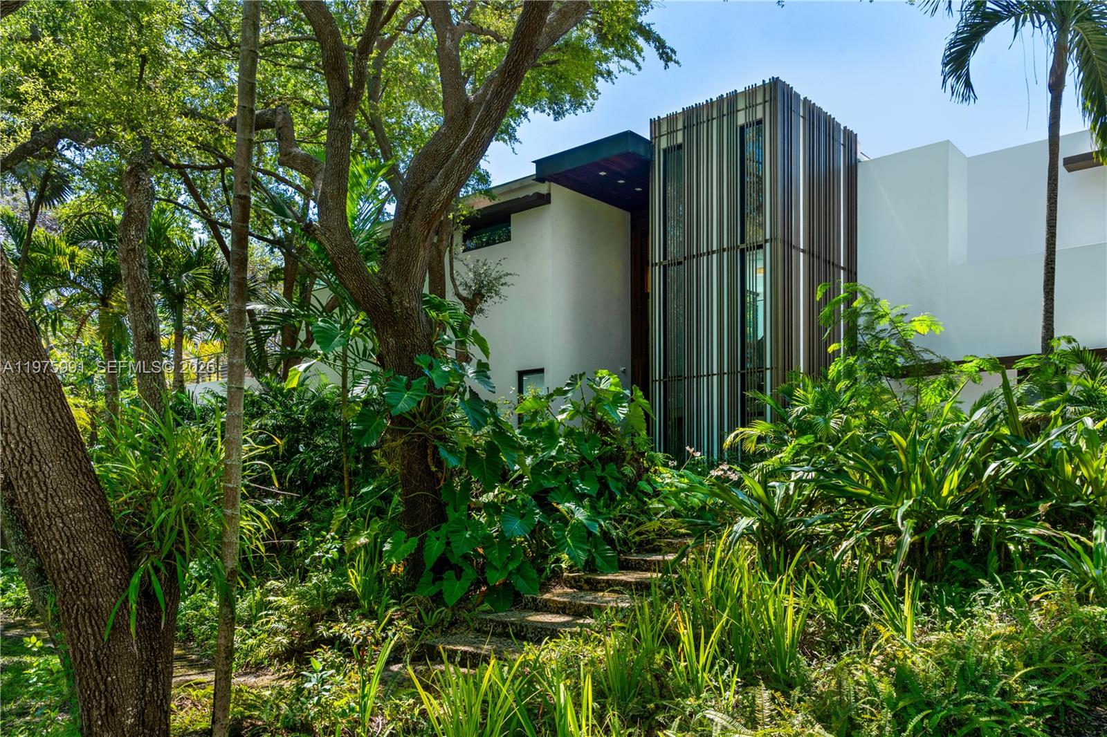 A modern house with a vertical slat facade is surrounded by lush tropical landscaping — 12220 Rock Garden Ln, Pinecrest FL 33156, PINECREST, FL