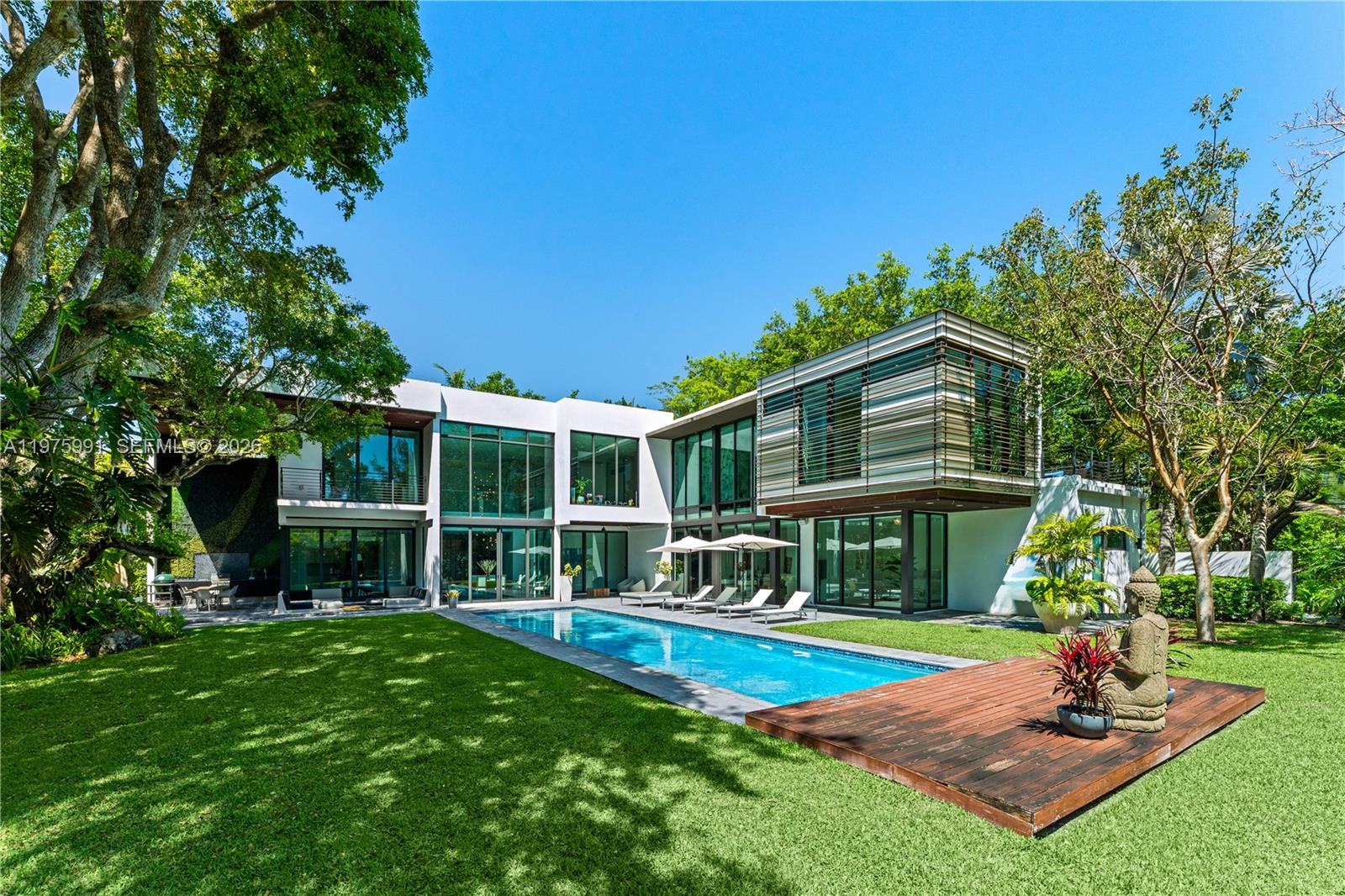A modern two-story house with floor-to-ceiling windows overlooks a rectangular swimming pool and lawn — 12220 Rock Garden Ln, Pinecrest FL 33156, PINECREST, FL