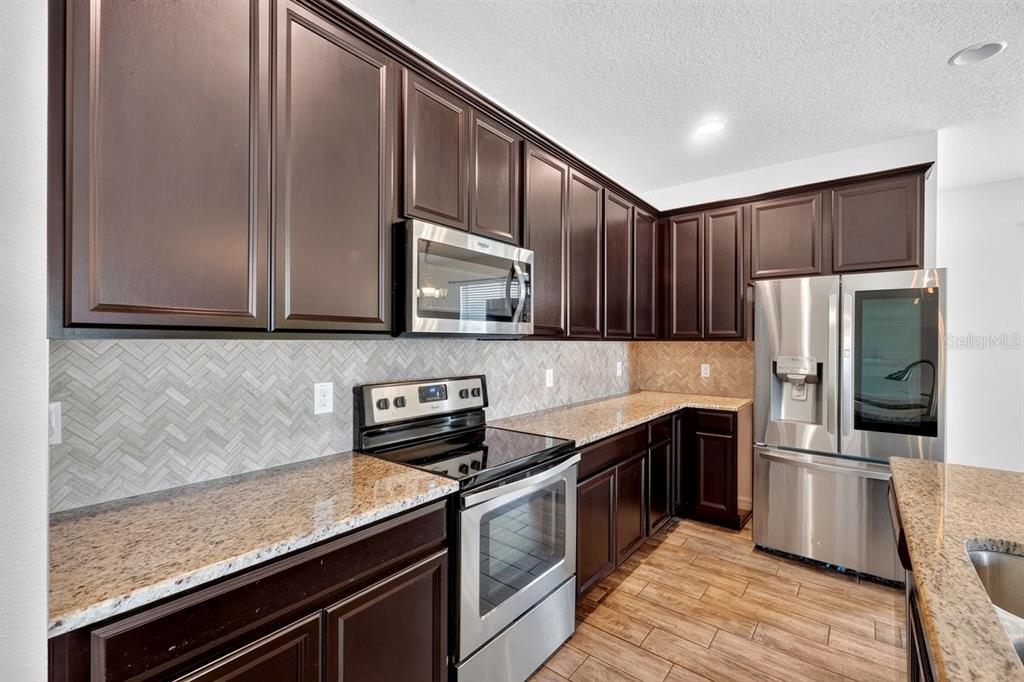 A kitchen with dark wood cabinets, granite countertops, stainless steel appliances, and a herringbone backsplash — 3833 LOON LANE, SANFORD, FL